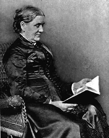 black and white image of mature woman sitting wicker chair reading a book.